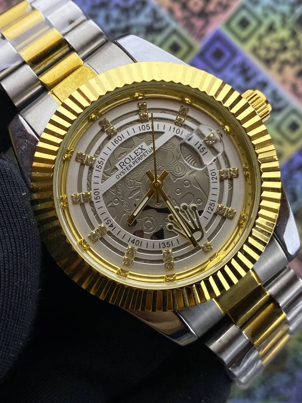 Gold and silver watch with intricate design on a colorful patterned background