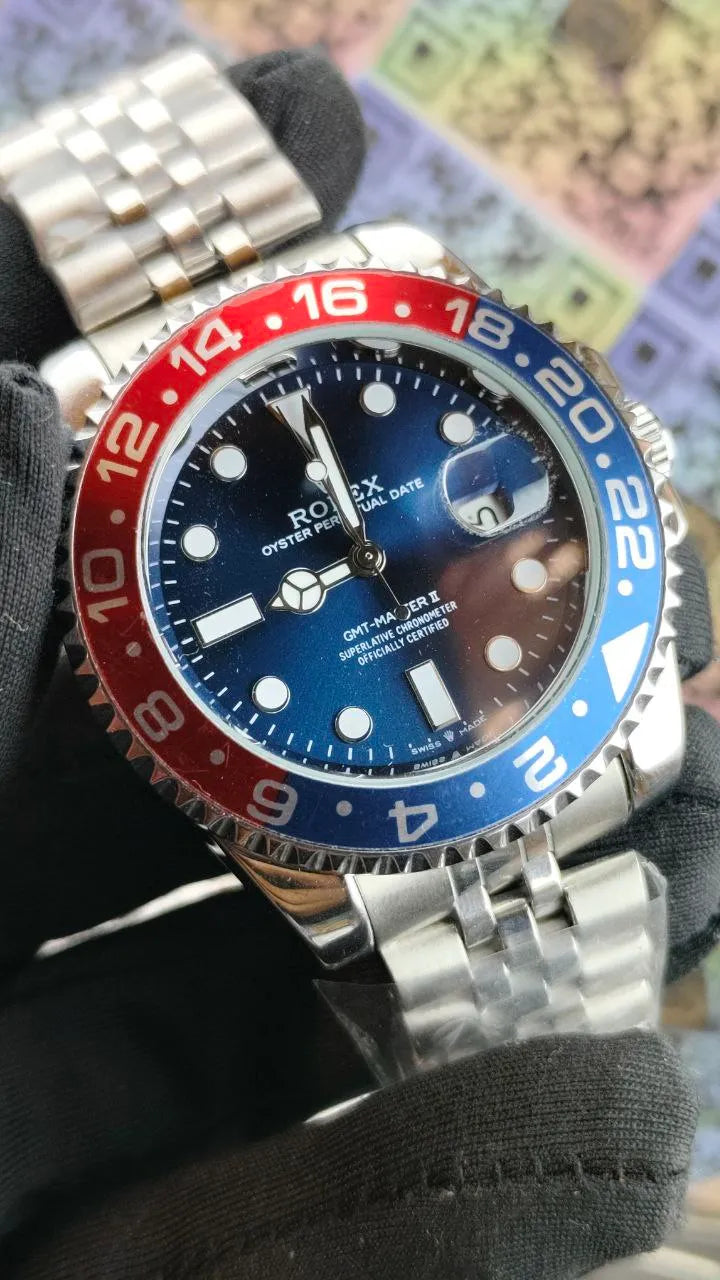 Close-up of a Rolex watch with a red and blue bezel on a textured surface.