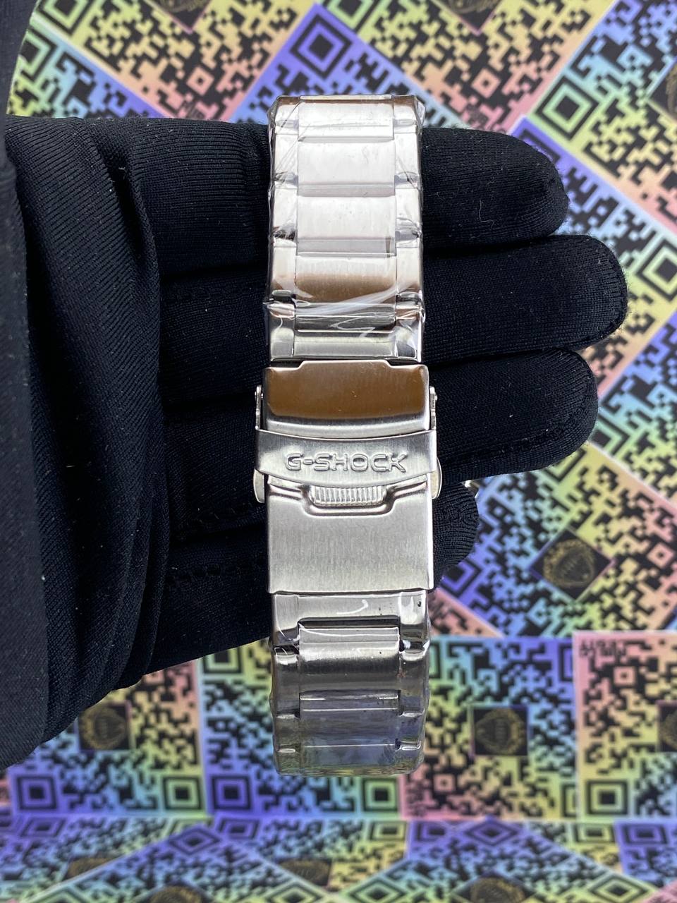 Silver G-Shock watch on a wrist with a colorful geometric pattern background