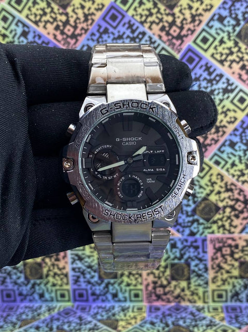 Silver Casio G-Shock watch held by a gloved hand against a colorful geometric pattern background.