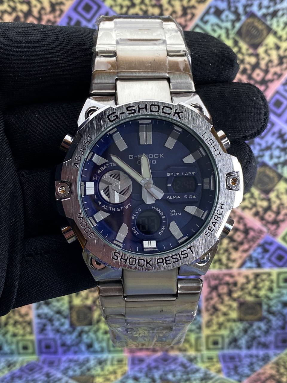 Silver Casio G-Shock watch on a black background with colorful pattern