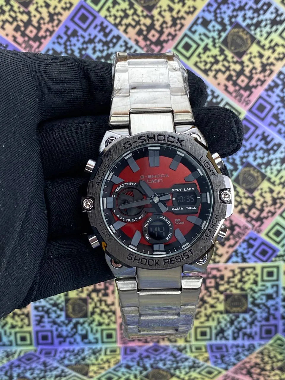 G-Shock watch held by a gloved hand against a colorful geometric pattern background