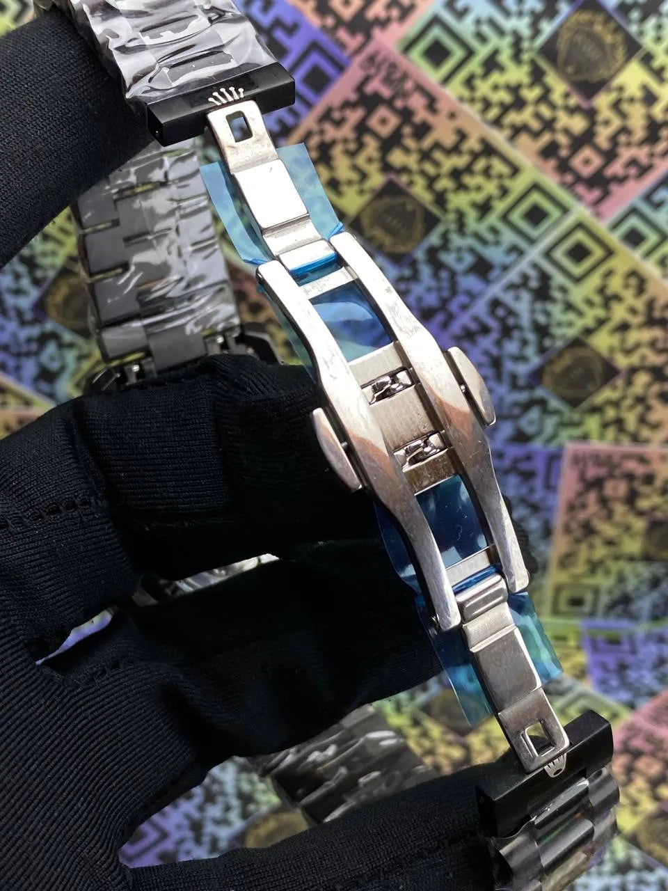 Close-up of a silver watch band with a colorful geometric pattern in the background